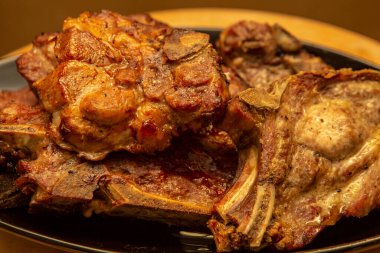 Siyah oval tabakta ızgara domuz pirzolası ve sarı ahşap masa.