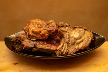 Siyah oval tabakta ızgara domuz pirzolası ve sarı ahşap masa.