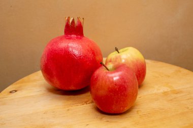 Kırmızı nar ve sarı bir zemin üzerinde ahşap bir masada iki kırmızı sarı elma.