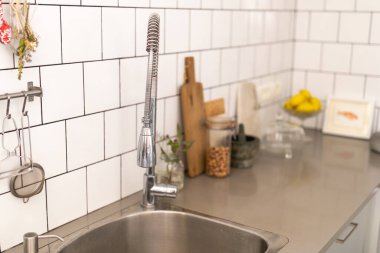 Lavabo, musluk, kesme tahtası, havan ve diğer mutfak malzemelerinin bulunduğu beyaz fayanslı bir mutfak atölyesi.