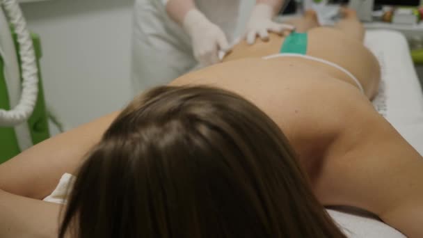 Женщина лежит на диване косметолога и получает массаж ягодиц и бедер — стоковое видео