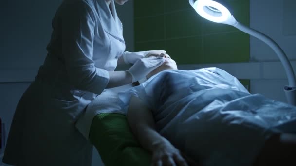 ब्यूटीशियन चमकदार दीपक के नीले प्रकाश में त्वचा देखभाल उपचार के लिए ग्राहकों के चेहरे को साफ करता है — स्टॉक वीडियो