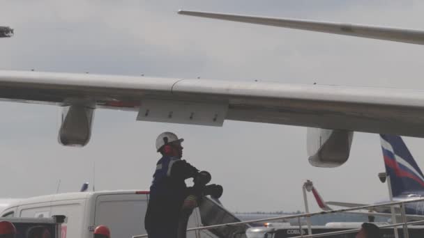 Homem de uniforme e capacete junta-se a uma mangueira para asa da aeronave para reabastecimento — Vídeo de Stock