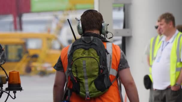 MOSCOU, RUSSIE - 25 JUILLET 2018 : Homme en casque et gilet orange haute visibilité marche sur la rampe d'accès de l'aéroport sous la pluie. Sac à dos Noerdway sur le dos — Video