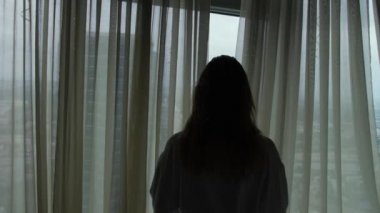 Bornoz kadın otel odasında perdeleri açıklayacak ve cityscape pencereden bakmak