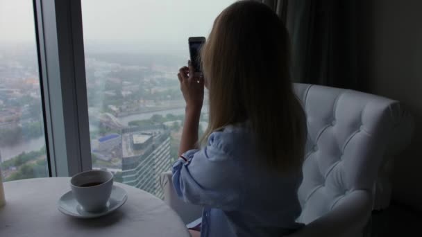 Mujer hace una foto de la vista de Moscú lluvioso en el teléfono celular sentado en la cafetería — Vídeos de Stock