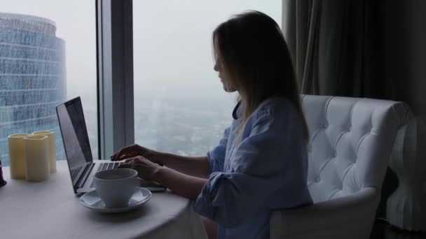 Tipos de mujer en la computadora portátil. Vista del paisaje urbano lluvioso desde la ventana del rascacielos — Vídeos de Stock