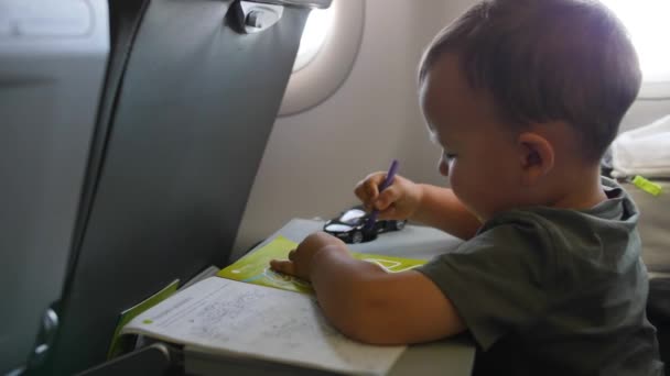 Малыш рисует сидя на пассажирском сидении в самолете. Маленький путешественник на борту — стоковое видео