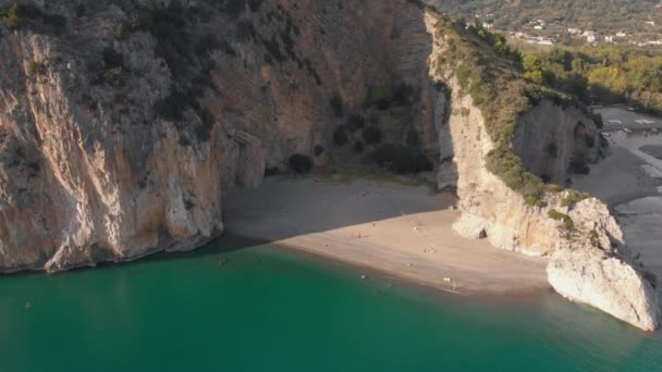 Sandy beach between steep rocks. Mediterranean coastline in sunny day. Aerial, camera moves away — Stock Video
