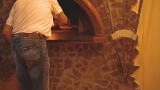 İtalyan Şef pizza peel kullanarak geleneksel odun ateşinde taş fırına koyar. — Stok video