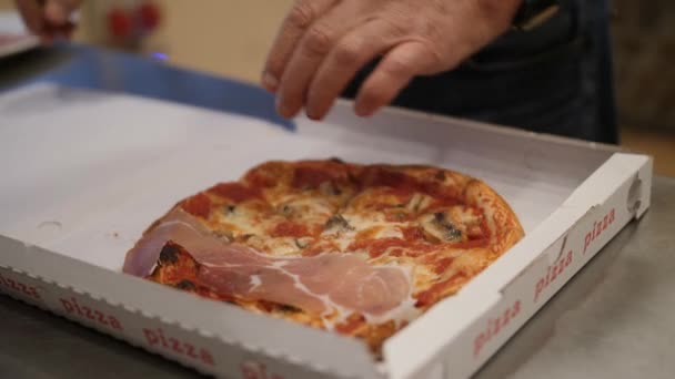 Man puts pieces of bacon on the hot pizza. Italian food in takeout box — Stock Video