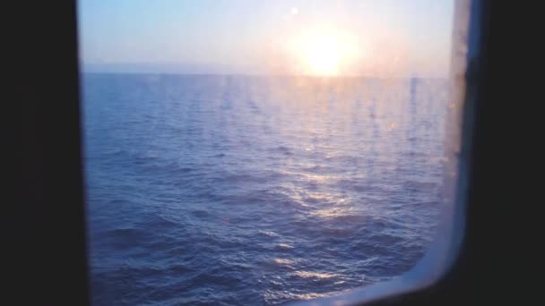 Sunrise above the blue sea. View from ferry boat porthole on waves reflecting sun light — Stock Video