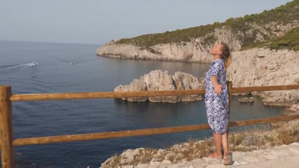 Giovane bella donna a braccia aperte, saluta il sole contro la costa rocciosa del mare blu. Capri, Italia — Video Stock