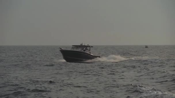 Pequeño barco a motor negro flota en las olas del mar dejando pista de espuma blanca — Vídeo de stock