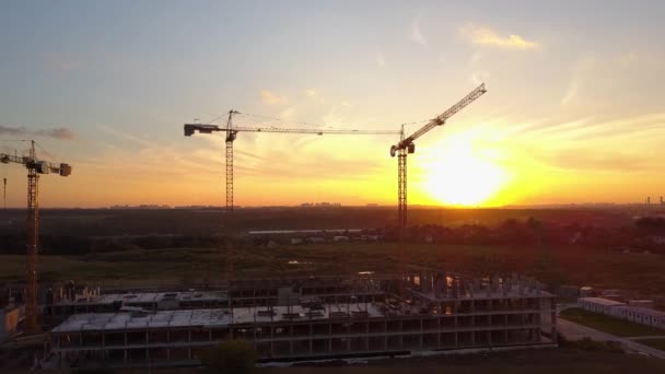 Χτίζοντας γερανοί στο εργοτάξιο ενάντια στον ουρανό του ηλιοβασιλέματος. Εναέρια βολή — Αρχείο Βίντεο
