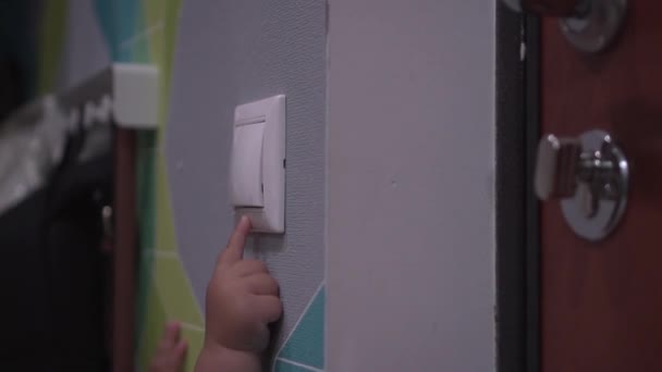 El bebé apaga el interruptor de una pared y se apagan las luces. Primer plano de la mano de los niños — Vídeo de stock