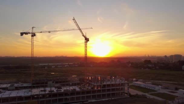 Tiro aéreo de guindastes sobre a construção em construção contra o céu brilhante por do sol — Vídeo de Stock