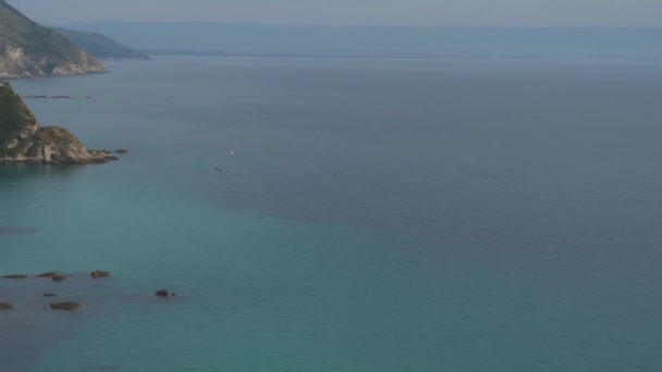 Seagulls soar over clear sea waters along mountainous sea shore with houses on slopes — Stock Video