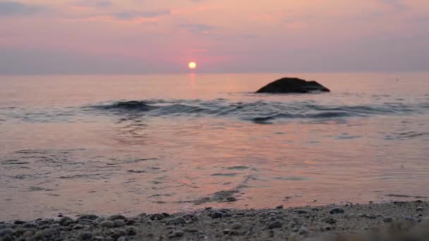 Cielo rosado al atardecer sobre el mar. Las olas ruedan sobre la arena y los guijarros en la costa — Vídeos de Stock