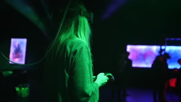 Egy nő a virtuális valóság headsetben joystickkal. A fény színe változik. — Stock videók
