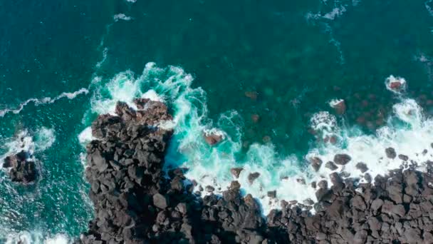 Onde schiumose rotolano su grandi pietre nere sulla riva dell'oceano blu. Aereo rallentatore colpo — Video Stock