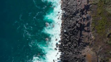 Kayalık bir deniz kıyısındaki yol. Mavi okyanus dalgaları taşların üzerinde beyaz köpüğe dönüşür. Perili, Azores