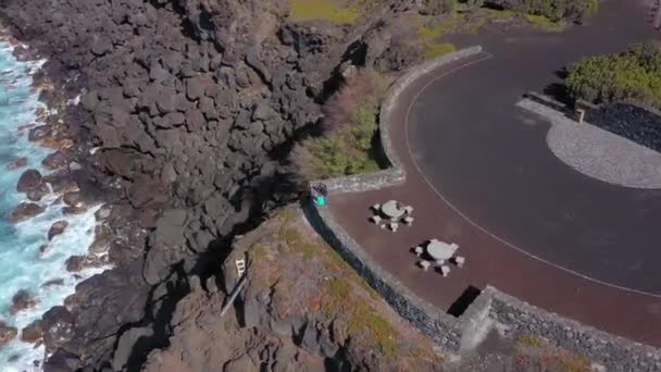 Deux personnes regardent l'océan assis au point de vue au-dessus des pierres noires. Varaduro do comprido, Faial, Açores — Video