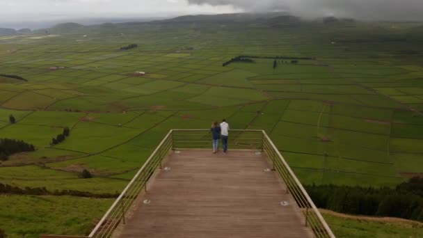 Par de pessoas no miradouro da Serra do Cume. Vale verde dividido em campos no sopé da montanha. Aviação da Terceira, Açores — Vídeo de Stock