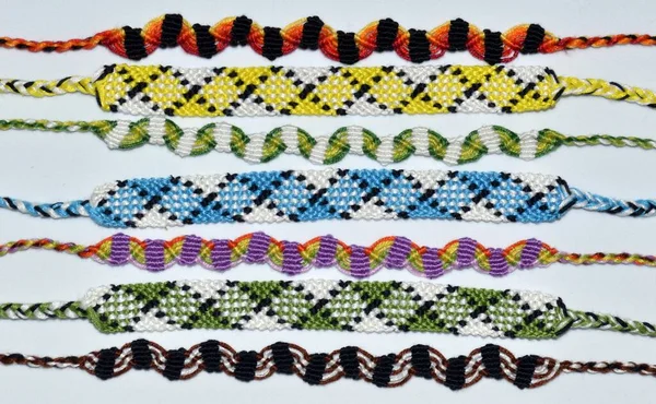 Multi-colored woven friendship bracelets handmade of embroidery bright thread with knots on light gray background