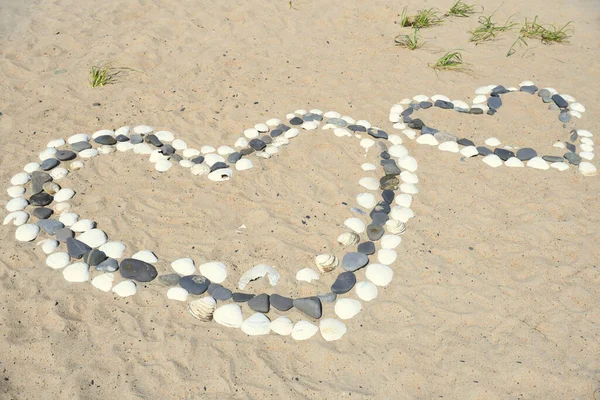One big heart made of stones and white seashells next to small heart on beach of the Japanese sea.