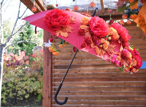 Creative idea for decorating a holiday, garden or backyard. Old worn-out umbrella with glued artificial flowers and leaves, suspended from the ceiling.