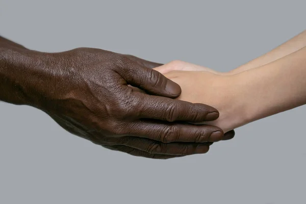 검은 수컷의 손은 사람의 하얀 손을 손바닥에 쥐고 있다. 인종간의 우정, 사랑, 존중, 인종 차별 과의 싸움이라는 개념. 우주의 복사, 회색 외진 배경. — 스톡 사진