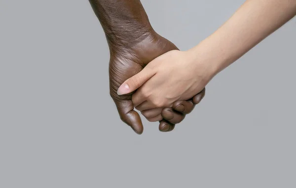 Uma mão masculina preta segura uma mão feminina branca. A mão de pele escura está localizada atrás. O conceito de amizade interracial, amor e respeito.Cópia do espaço, fundo isolado cinza . — Fotografia de Stock