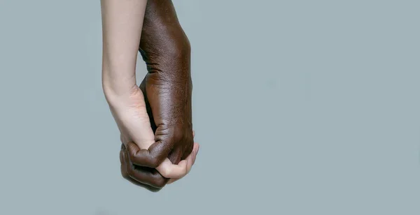 Siyah bir adam beyaz bir kadının elini tutuyor ve parmaklarını birbirine dokuyor. Irklar arası arkadaşlık, sevgi ve saygı kavramı. Mekanın kopyası, gri yalıtılmış arka plan, kenar görüş, pankart..