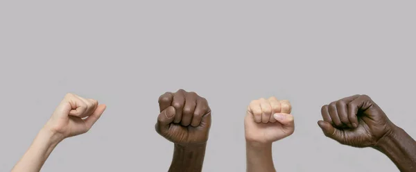 Μαύρα και λευκά ανθρώπινα χέρια με υψωμένες γροθιές στον αέρα σε ένα γκρίζο απομονωμένο φόντο. Κοντινό πλάνο, πανό, αντίγραφο χώρου. Η έννοια της διαμαρτυρίας, της βίας και του αγώνα. — Φωτογραφία Αρχείου