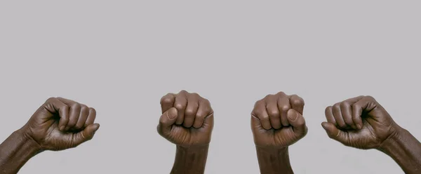 Gri izole bir arka planda havaya kaldırılmış yumrukları olan siyah Afro-Amerikan insan elleri. Yakın çekim, pankart, kopyalama alanı. Protesto, şiddet ve mücadele kavramı.