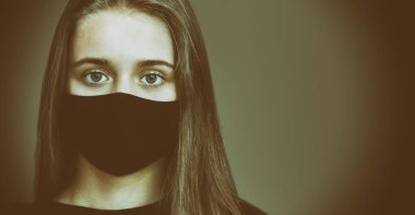 Siyah bir tıbbi maske takmış genç bir kızın portresi. COVID-19 virüs salgınına karşı koruma kavramı. Yakın plan, kopyalama alanı.