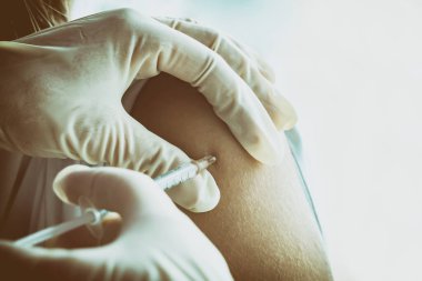 Doktor, hastanın omzunda aşı yapar. Kadın. Nüfusun gribe ve koronavirüse karşı rutin aşı konsepti. Seçici odaklanma, boşluk kopyalama, yakın plan.