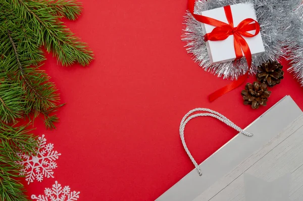 Christmas Flatley. Ramos de pinheiro, flocos de neve brancos, uma caixa de presente com um arco vermelho e um saco de compras. Fundo vermelho, vista superior, espaço de cópia — Fotografia de Stock