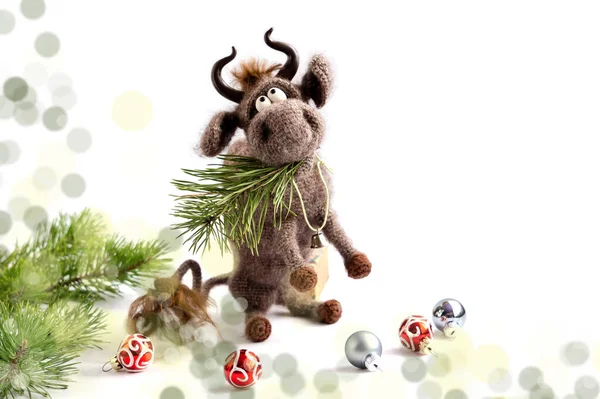おもちゃの雄牛 雄牛は2021年のシンボルです 白い背景に毛糸で編んだ茶色いおもちゃの雄牛が後ろ足に座り 口の中に松の枝がある コピースペース 選択的フォーカス — ストック写真