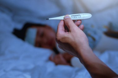 için termometre ile yüksek ateş izlemek için gece yatak odasında hasta küçük kızın termometre ön planda tutan baba, Çocuk için sıcaklık aşağı getirmek için yüksek ateş ve ılık sponging vardı