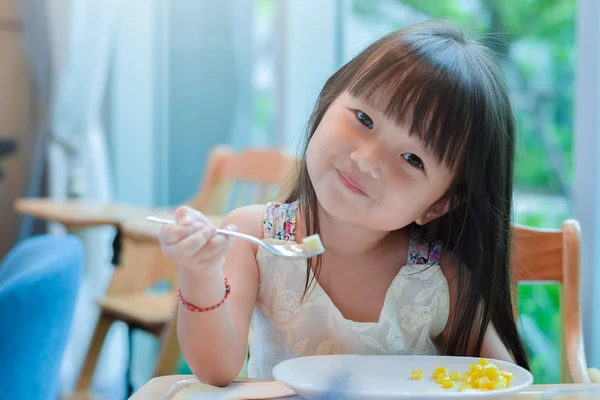 Маленькая азиатская девочка завтракает по утрам со счастливым улыбающимся лицом и показывает еду на ложке . — стоковое фото