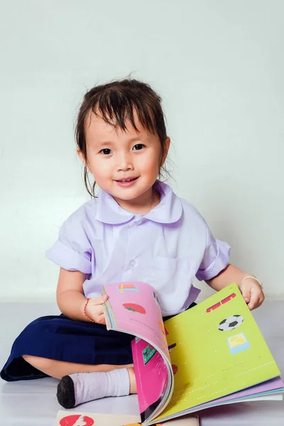 Klein meisje het lezen van een boek ze dragen Preschool schooluniformen in huis. — Stockfoto