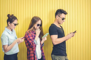 Sarı duvara akıllı telefon kullanarak genç arkadaş grubu, mobil akıllı telefon kavramı bağımlısı insanlar