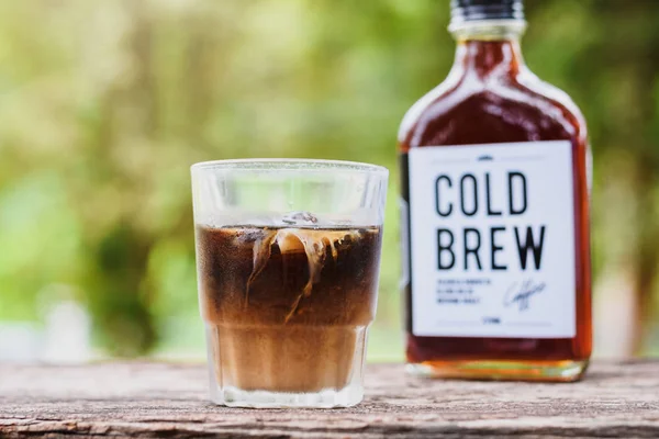 Cold brew coffee with milk on a table outside with cold-brew coffee in a glass bottle for take away