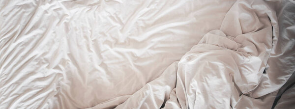 Top view of soft bedding sheets and blanket messed up after nights sleep ,comfort sleep on bedding in a hotel room, concept travel and vacation for wide banner background.