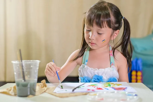 Asian little girl child painting with paintbrush and colorful paints on paper doing school home work Drawing and painting at home.