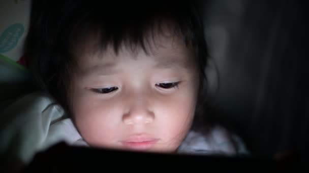 目を閉じて女の子は夜にベッドの上でタブレットでビデオを見ているライトが画面から反射点滅し、中毒や漫画の概念を持つゲームを使用して子供たち — ストック動画