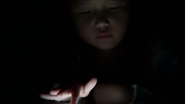 Küçük kız ekranı kaldırır ve gece yatağında video izlerler. Ekrandan yansıyan ışıklar, bağımlılık ve çizgi film oyunları oynayan çocuklar. — Stok video