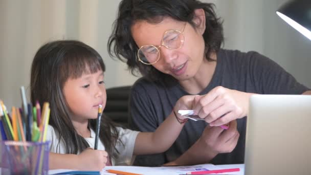 Padre usando el ordenador portátil hacer horas extras y la hija haciendo la tarea de la escuela en la mesa de trabajo ofiice en casa por la noche — Vídeos de Stock